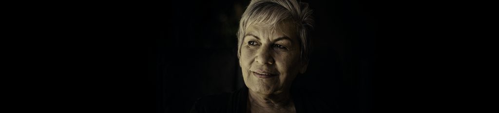 An old woman with short blonde hair against a black background